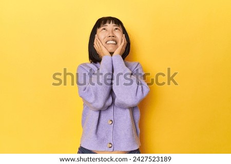 Young Chinese lady, yellow studio background whining and crying disconsolately.