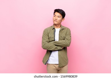 young chinese man doubting thinking  biting lip   feeling insecure   nervous  looking to copy space the side against flat color wall