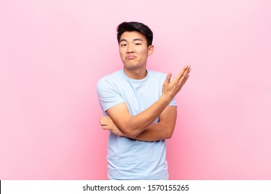 Young Chinese Man Feeling Confused And Clueless, Wondering About A Doubtful Explanation Or Thought Against Flat Color Wall