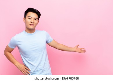 Young Chinese Man Feeling Happy And Cheerful, Smiling And Welcoming You, Inviting You In With A Friendly Gesture Against Flat Color Wall