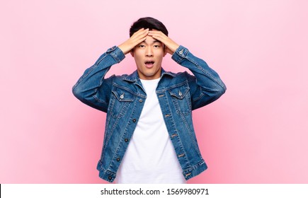 Young Chinese Man Feeling Horrified And Shocked, Raising Hands To Head And Panicking At A Mistake Against Flat Color Wall