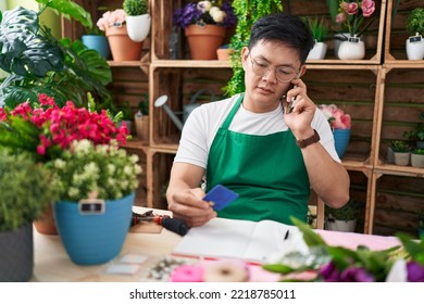 Young Chinese Man Florist Talking On Smartphone Holding Credit Card At Flower Shop