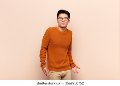 young chinese man and goofy  crazy  surprised expression  puffing cheeks  feeling stuffed  fat   full food against flat color wall