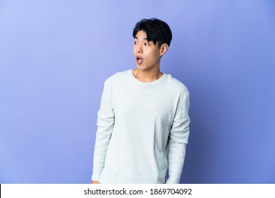 Young Chinese Man Isolated On Purple Background Doing Surprise Gesture While Looking To The Side