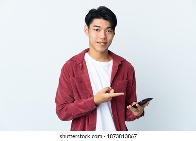 Young Chinese Man Isolated On White Background Using Mobile Phone And Pointing It