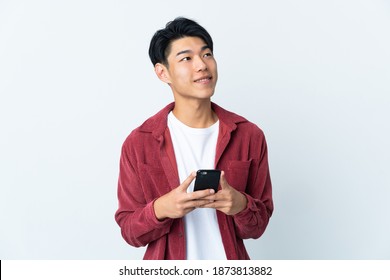 Young Chinese Man Isolated On White Background Using Mobile Phone And Looking Up