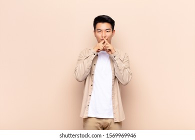 young chinese man looking serious   displeased and both fingers crossed up front in rejection  asking for silence against flat color wall