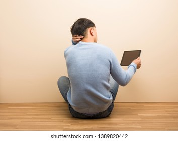 Young chinese man sitting using his tablet from behind thinking about something