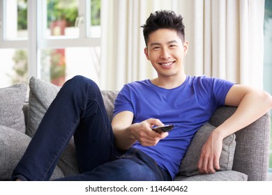 Young Chinese Man Sitting And Watching TV On Sofa At Home