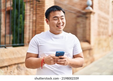 Young Chinese Man Smiling Confident Using Smartphone At Street