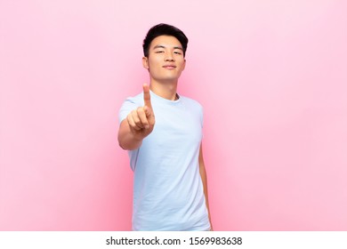 young chinese man smiling proudly and confidently making number one pose triumphantly, feeling like a leader against flat color wall - Shutterstock ID 1569983638