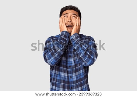 Young Chinese man in studio background whining and crying disconsolately.