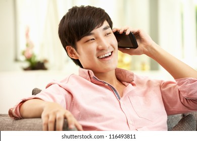 Young Chinese Man Using Mobile Phone On Sofa At Home