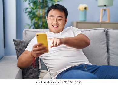 Young Chinese Man Using Smartphone Sitting On Sofa At Home