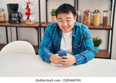 Young Chinese Man Using Smartphone Sitting On Table At Home