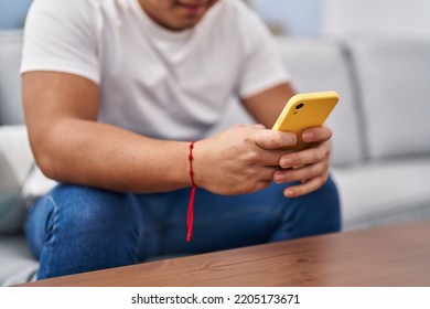 Young Chinese Man Using Smartphone Sitting On Sofa At Home