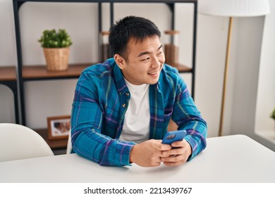 Young Chinese Man Using Smartphone Sitting On Table At Home