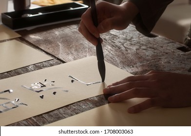 A young chinese is practicing her calligraphy using a brush, black ink and traditional paper:
財→assets 
源→source
And the meaning of the 2 simbols is 