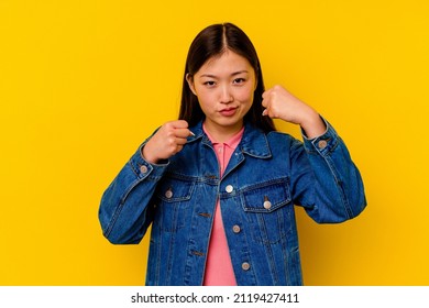 Young chinese woman isolated on yellow background throwing a punch, anger, fighting due to an argument, boxing.