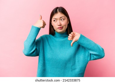 Young Chinese Woman Isolated On Pink Background Showing Thumbs Up And Thumbs Down, Difficult Choose Concept