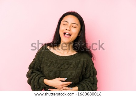 Young chinese woman isolated on a pink background laughs happily and has fun keeping hands on stomach.