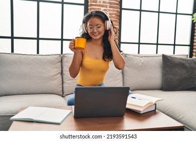 Young Chinese Woman Listening To Music Using Laptop Sitting On Sofa At Home