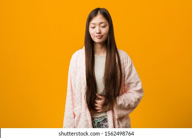 Young chinese woman in pajama touches tummy, smiles gently, eating and satisfaction concept.