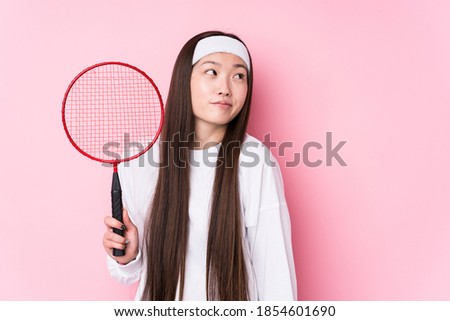 Young chinese woman playing badminton isolated dreaming of achieving goals and purposes