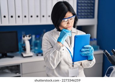 Young chinese woman scientist using touchpad working at laboratory