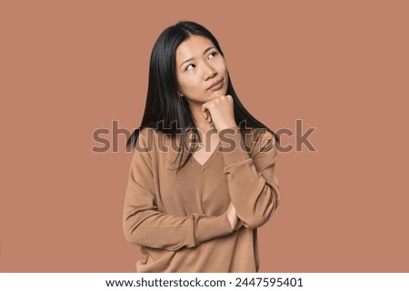 Young Chinese woman in studio setting thinking and looking up, being reflective, contemplating, having a fantasy.