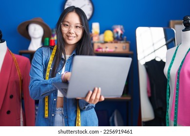 Young chinese woman tailor smiling confident using laptop at clothing factory - Shutterstock ID 2256919461