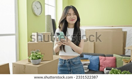 Young chinese woman using smartphone standing at new home