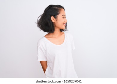 Young chinese woman wearing casual t-shirt standing over isolated white background looking away to side with smile on face, natural expression. Laughing confident.