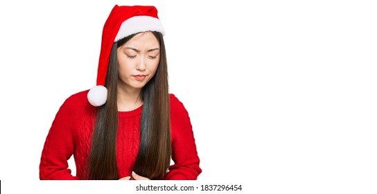 Young Chinese Woman Wearing Christmas Hat With Hand On Stomach Because Indigestion, Painful Illness Feeling Unwell. Ache Concept. 