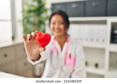 Young Chinese Woman Wearing Doctor Uniform Holding Heart At Clinic