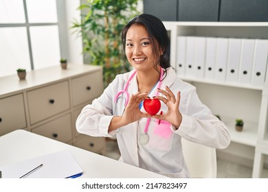 Young Chinese Woman Wearing Doctor Uniform Holding Heart At Clinic