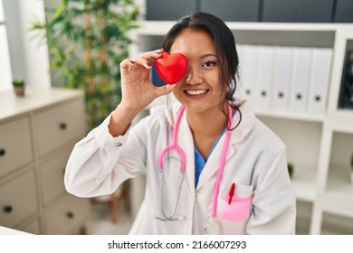 Young Chinese Woman Wearing Doctor Uniform Holding Heart Over Eye At Clinic