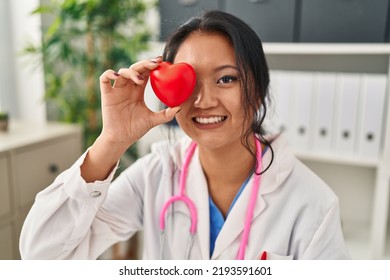 Young Chinese Woman Wearing Doctor Uniform Holding Heart Over Eye At Clinic