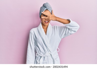 Young Chinese Woman Wearing Shower Towel Cap And Bathrobe Peeking In Shock Covering Face And Eyes With Hand, Looking Through Fingers With Embarrassed Expression. 