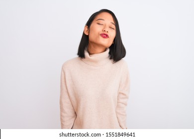 Joven china con suéter de cuello alto sobre fondo blanco aislado mirando a la cámara sonando un beso en el aire siendo adorable y sexy. Expresión de amor.