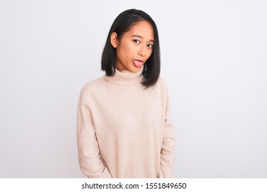 Joven china con suéter de cuello alto sobre un fondo blanco aislado que saca la lengua alegre con expresión graciosa. Concepto de emoción.