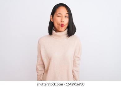 Joven china con suéter de cuello alto sobre fondo blanco aislado haciendo cara de pez con labios, gesto loco y cómico. Expresión divertida.