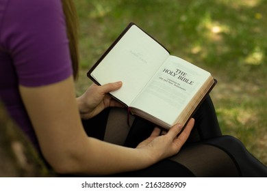 Young Christian Woman Holding And Reading An Open Holy Bible Book In Peace In Nature. Studying And Searching The Scripture, Praying To God Jesus Christ, Sabbath Rest Biblical Concept.