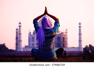 Young christian woman in traditional indian clothes in front of Taj Mahal in Agra, India makes yoga exercises. UNESCO World Heritage Site. Mosque. Mausoleum. Meditation.