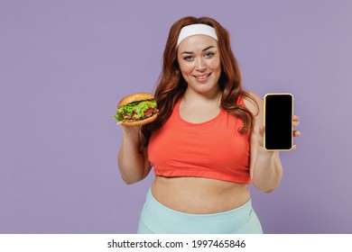 Young Chubby Overweight Plus Size Fat Fit Woman In Red Top Warm Up Training Hold Fast Food Burger Use Mobile Cell Phone Blank Screen Workspace Isolated On Purple Background Gym. Workout Sport Concept.