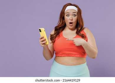 Young Chubby Overweight Plus Size Big Fat Fit Woman In Red Top Warm Up Training Point Index Finger On Yoga Mat Mobile Cell Phone Isolated On Purple Background Home Gym Workout Sport Motivation Concept