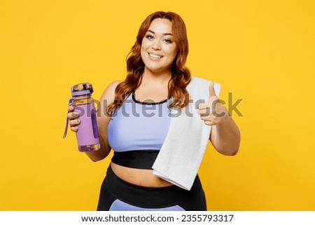 Young chubby overweight plus size big fat fit woman wear blue top warm up train hold towel bottle drink water show thumb up isolated on plain yellow background studio home gym. Workout sport concept