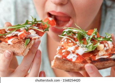 Young chubby woman sitting at table in kitchen binge eating eating slices of pizza fast hungry mouth close-up