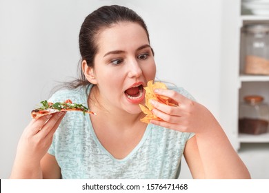 Young Chubby Woman Sitting At Table In Kitchen Binge Eating Eating Slice Of Pizza And Chips Hungry Close-up