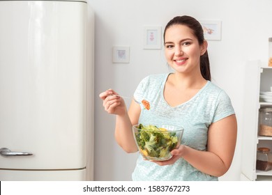 Young Chubby Woman Standing In Kitchen Holding Bowl Eating Green Healthy Salad Looking Camera Smiling Cheerful